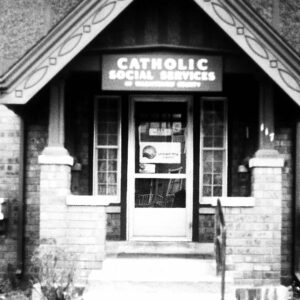 Old, black and white photo of the original Catholic Social Services of Washtenaw County, located in a house with a stone facade and porch.