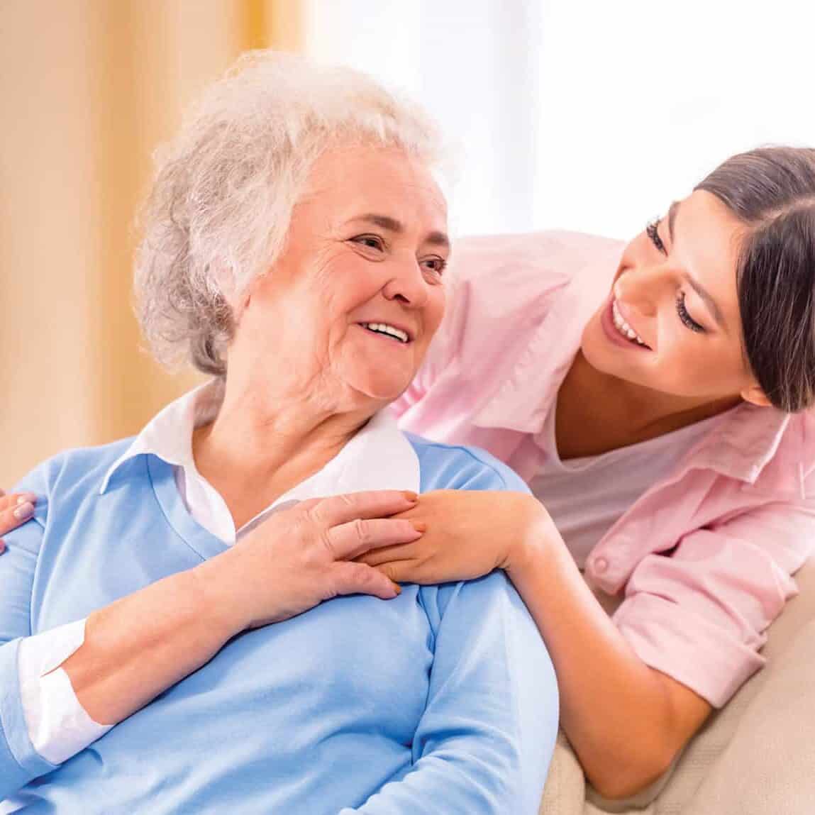 An older woman smiling at a younger woman with her arms around her shoulders.